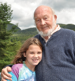 Robert Preyer with great-granddaughter Maggie Preyer Friedman Man with a beard poses with a little girl, with mountains, trees and clouds in the background